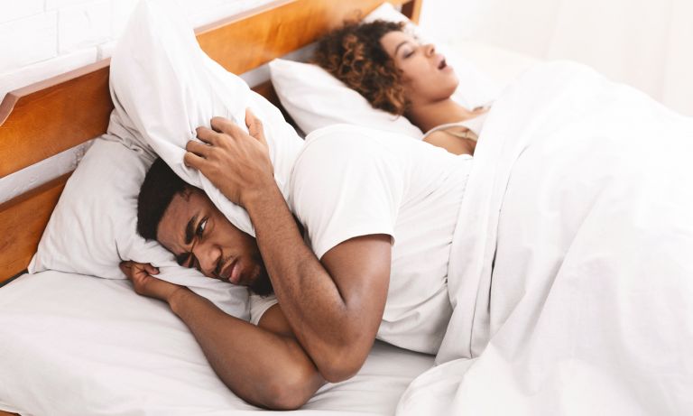 man covers ears while woman snores 768